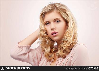 fresh and pretty young girl wearing a pink shirt and with curly hairstyle on her blond long hair looking at the camera with lovely pose against white background