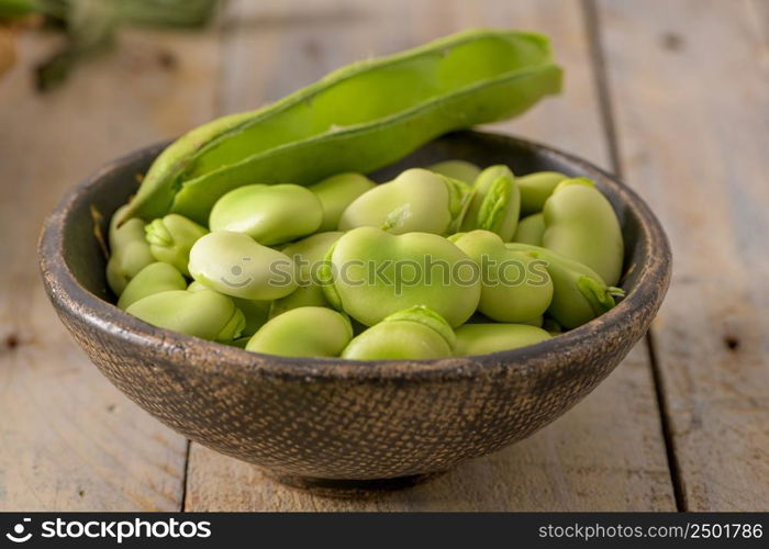 Fresh and raw green broad beans on wooden table.