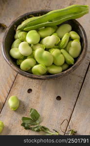 Fresh and raw green broad beans on wooden table.