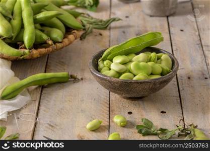Fresh and raw green broad beans on wooden table.