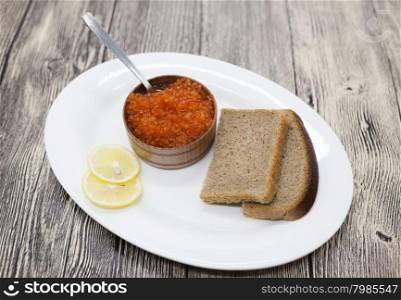 Fresh appetizing red salmon caviar in a wooden jar with pieces of bread on a porcelain platter.. Fresh appetizing red salmon caviar in a wooden jar with pieces of bread on a porcelain platter