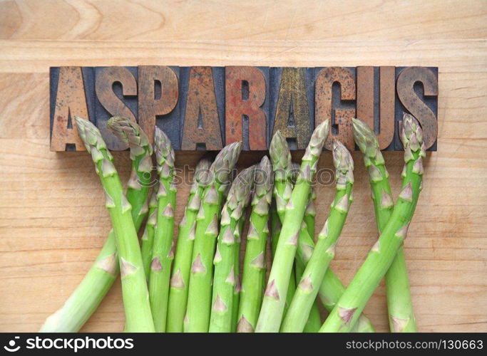 Fresh asparagus  on a cutting board with the word asparagus in old wood type