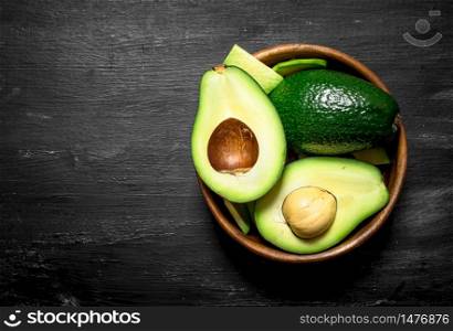 Fresh avocado in a bowl. On a black wooden background. Top view.. Fresh avocado in a bowl. On black wooden background.