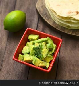 Fresh avocado salad prepared with lime juice, pepper, salt and garnished with fresh coriander leaves, homemade tortillas in the back (Selective Focus, Focus in the middle of the salad) . Avocado Salad