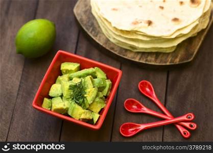 Fresh avocado salad prepared with lime juice, pepper, salt and garnished with fresh coriander leaves, homemade tortillas in the back (Selective Focus, Focus in the middle of the salad)