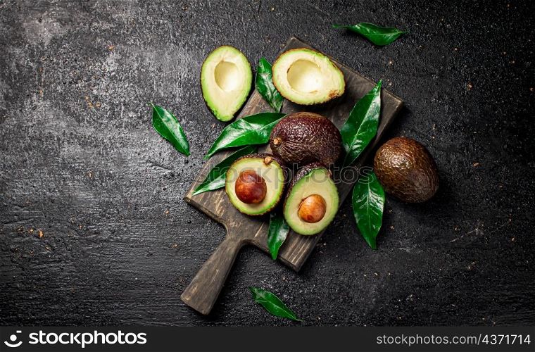 Fresh avocado with foliage on a cutting board. On a black background. High quality photo. Fresh avocado with foliage on a cutting board.