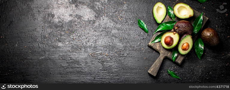 Fresh avocado with foliage on a cutting board. On a black background. High quality photo. Fresh avocado with foliage on a cutting board.