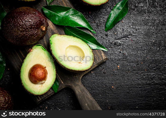 Fresh avocado with foliage on a cutting board. On a black background. High quality photo. Fresh avocado with foliage on a cutting board.