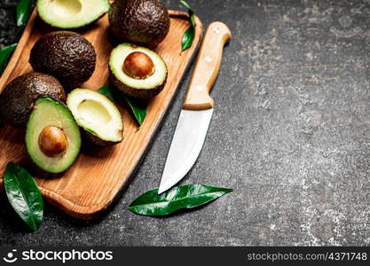 Fresh avocado with foliage on a cutting board. On a black background. High quality photo. Fresh avocado with foliage on a cutting board.