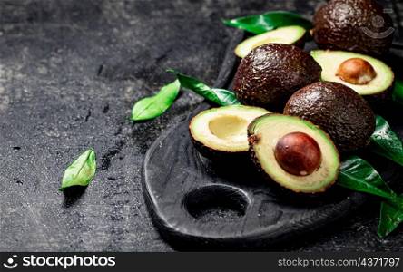 Fresh avocado with foliage on a cutting board. On a black background. High quality photo. Fresh avocado with foliage on a cutting board.