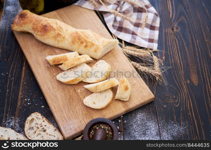 Fresh baguette and sliced bread on wooden cutting board at kitchen table.. Fresh baguette and sliced bread on wooden cutting board at kitchen table