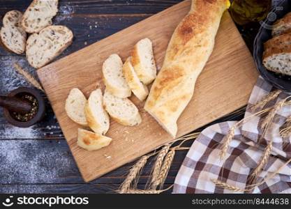 Fresh baguette and sliced bread on wooden cutting board at kitchen table.. Fresh baguette and sliced bread on wooden cutting board at kitchen table