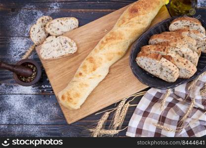 Fresh baguette and sliced bread on wooden cutting board at kitchen table.. Fresh baguette and sliced bread on wooden cutting board at kitchen table