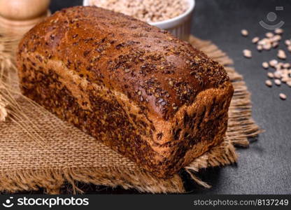 Fresh baked brown bread with ears and grains of wheat on a dark concrete background. Fresh baked brown bread with ears and grains of wheat