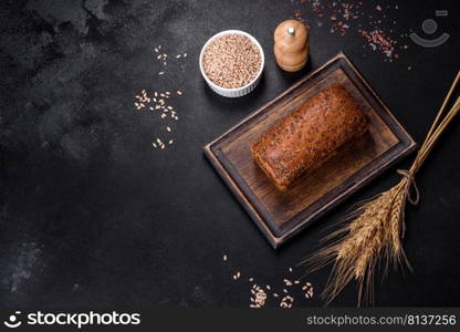 Fresh baked brown bread with ears and grains of wheat on a dark concrete background. Fresh baked brown bread with ears and grains of wheat