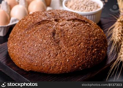 Fresh baked brown bread with ears and grains of wheat on a dark concrete background. Fresh baked brown bread with ears and grains of wheat