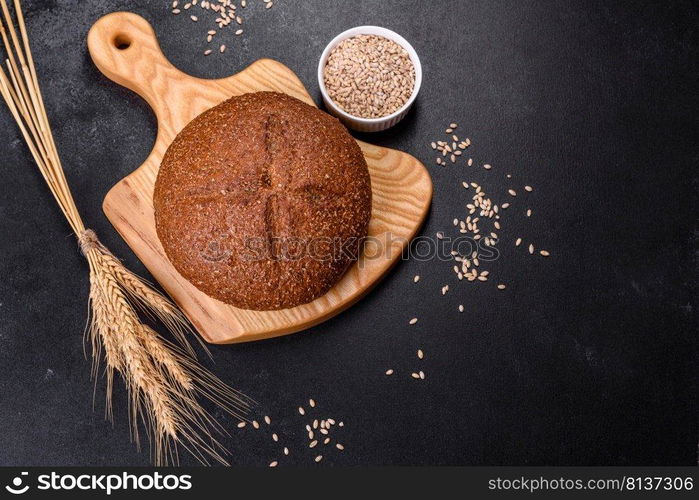 Fresh baked brown bread with ears and grains of wheat on a dark concrete background. Fresh baked brown bread with ears and grains of wheat