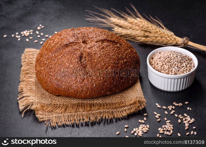 Fresh baked brown bread with ears and grains of wheat on a dark concrete background. Fresh baked brown bread with ears and grains of wheat