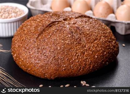 Fresh baked brown bread with ears and grains of wheat on a dark concrete background. Fresh baked brown bread with ears and grains of wheat