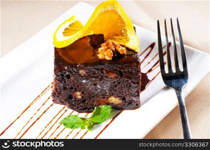 fresh baked delicious chocolate and walnuts cake with slice of orance on top and mint leaf