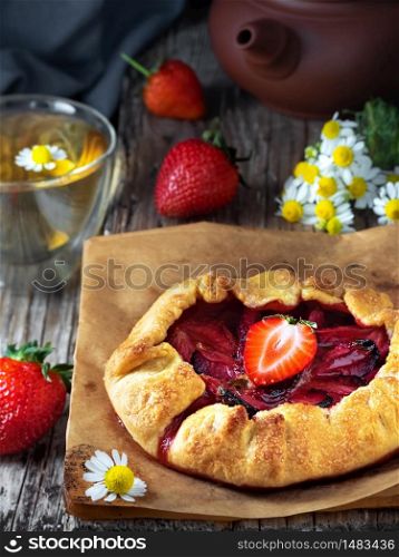 Fresh baked galette or open strawberry pie on a table, close up. Homemade cakes, fresh berries and a cup of chamomile tea