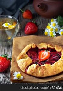 Fresh baked galette or open strawberry pie on a table, close up. Homemade cakes, fresh berries and a cup of chamomile tea