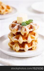 fresh baked waffles with syrup in a white plate on wooden background.