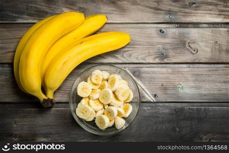 Fresh bananas and banana slices in a glass bowl. On a wooden background.. Fresh bananas and banana slices in a glass bowl.