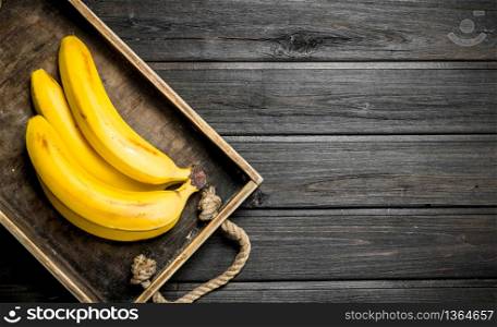 Fresh bananas in a wooden box. On a black wooden background.. Fresh bananas in a wooden box.