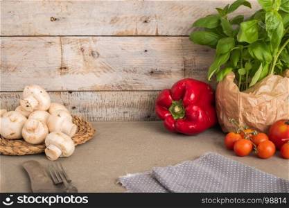 Fresh basil and other ingredients for Italian cuisine. Cherry tomatoes, basil and red pepper on wooden table for use as cooking ingredients