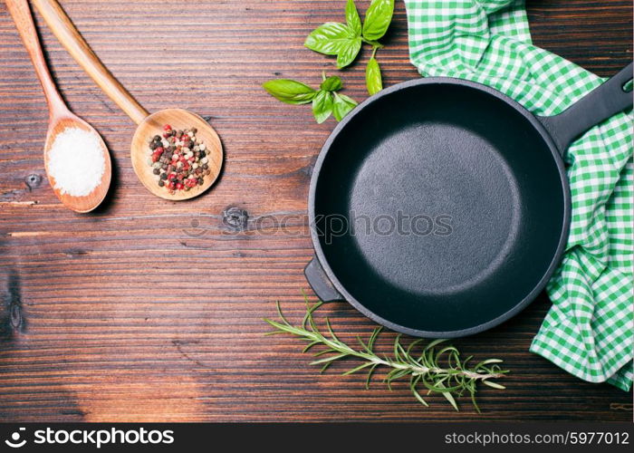 Fresh basil and rosemary, sea salt and dry peppercorns in wooden spoons near the frying pan