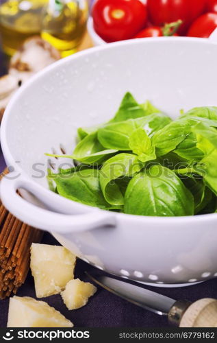 Fresh basil in colander and ingredients for making italian pasta