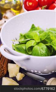 Fresh basil in colander and ingredients for making italian pasta