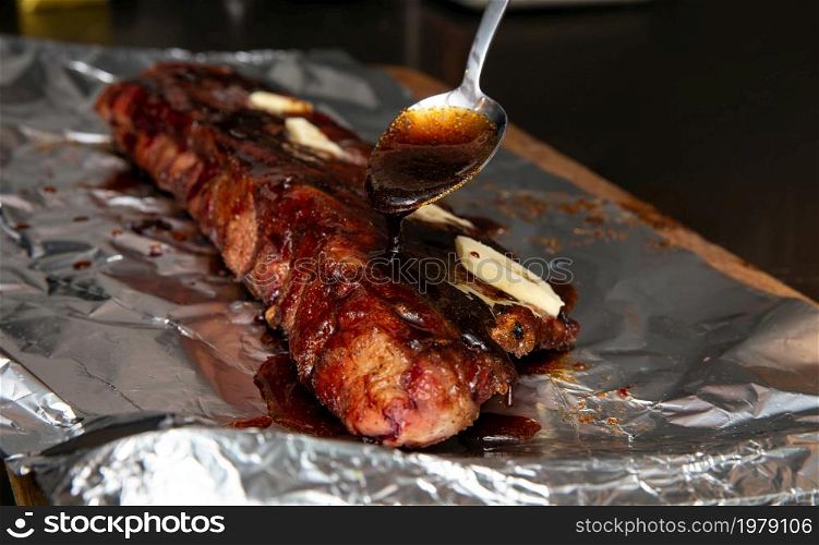 Fresh BBQ ribs, glazing sauce with spoon on pork ribs for sticky sugar result close up. Fresh BBQ ribs, glazing sauce with spoon on pork ribs for sticky sugar result