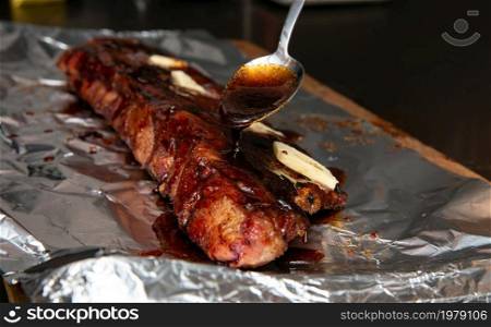 Fresh BBQ ribs, glazing sauce with spoon on pork ribs for sticky sugar result close up. Fresh BBQ ribs, glazing sauce with spoon on pork ribs for sticky sugar result