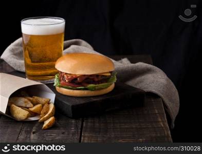 Fresh beef burger with potato wedges and glass of beer on wooden background