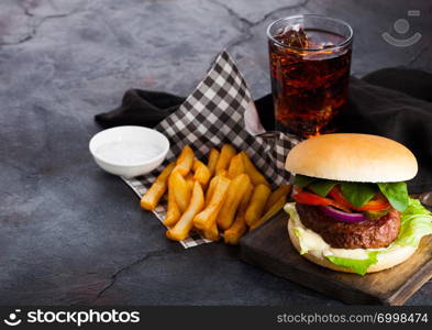 Fresh beef burger with sauce and vegetables and glass of cola soft drink with potato chips fries on stone kitchen background.