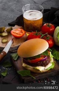 Fresh beef burger with sauce and vegetables and glass of lager craft beer with potato chips fries on stone kitchen background.