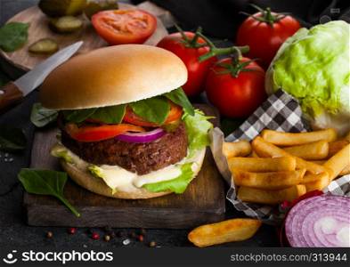 Fresh beef burger with sauce and vegetables and potato chips fries on stone kitchen table background.