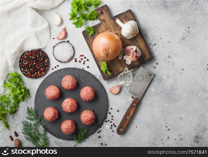 Fresh beef meatballs on stone board with pepper, salt and garlic on light background with dill,parsley and dill and onion. Top view