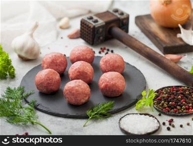 Fresh beef meatballs on stone board with pepper, salt and garlic on light background with dill,parsley and dill and onion.