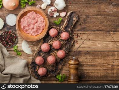 Fresh beef raw meatballs on wooden board with mince on bowl plate with pepper, salt and garlic on wooden background with parsley and dill with onion.