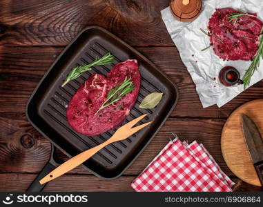 fresh beef steak with rosemary on a square frying pan, top view