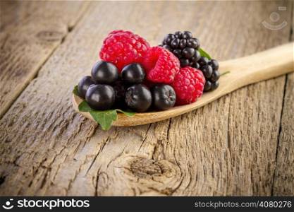 fresh berries in wooden spoon on wooden table