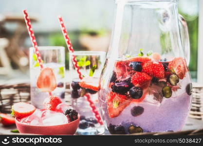 Fresh berries infused water with ice cubes in glass, close up, front view