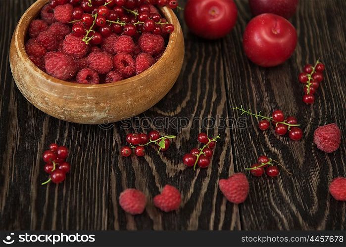 Fresh berries raspberry, red currant and plums on wooden table