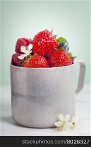 Fresh berry in old aluminum mug on white marble table with blue background