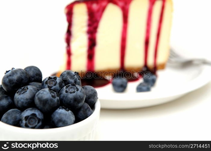 Fresh Blueberries And Cheesecake. Plain Cheesecake with a Blueberry sauce poured over the top with fresh berries on the plate next to the cake and topped with a mint leaf.