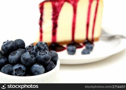 Fresh Blueberries And Cheesecake. Plain Cheesecake with a Blueberry sauce poured over the top with fresh berries on the plate next to the cake and topped with a mint leaf.