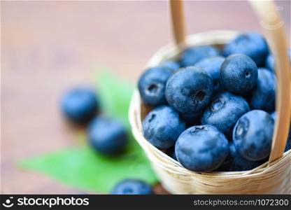 Fresh blueberries fruit in basket and green leaves on wooden background - selective focus